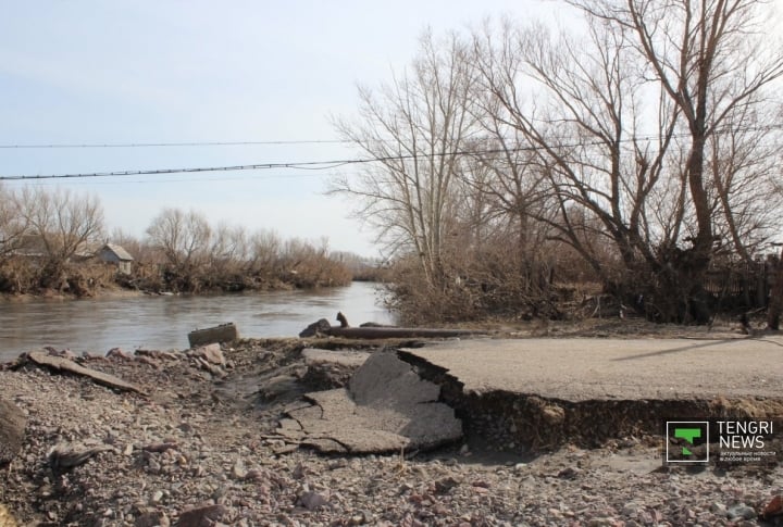 Вскрытый потоком воды асфальт, проложенный вдоль реки.