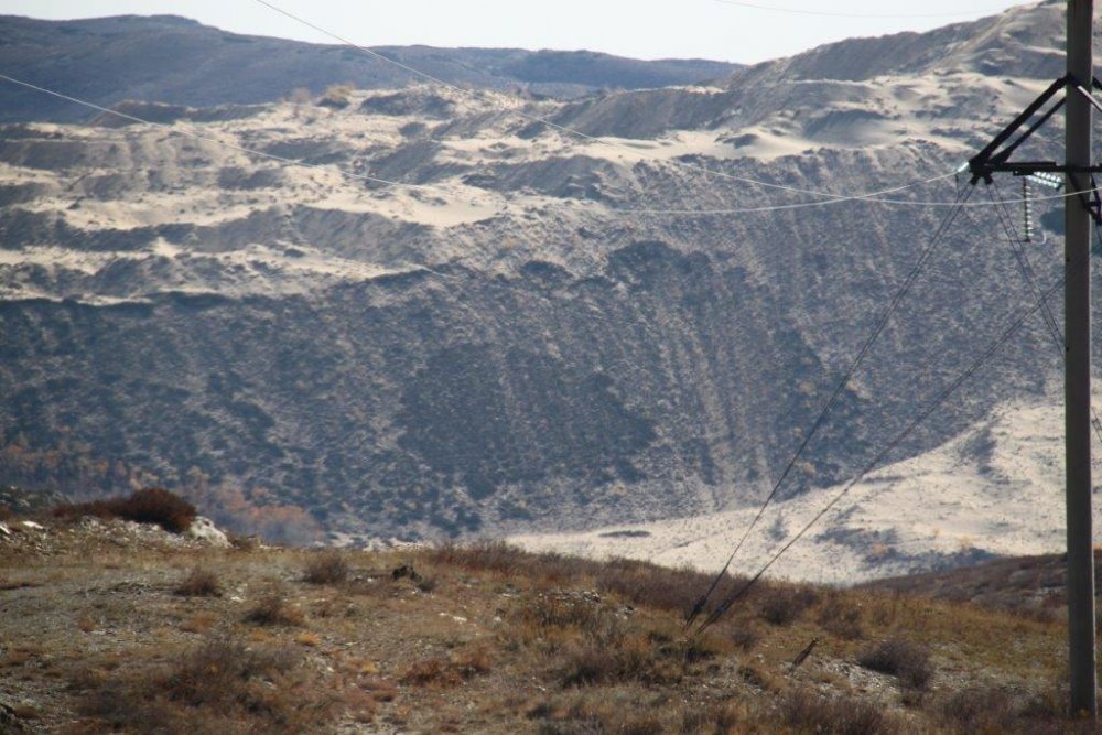 Это уникальное фото сделано на границе Казахстана и Китая. Склон дальней горы - это уже Китай. На казахстанской стороне есть растения, тогда как соседняя территория выглядит безжизненной.