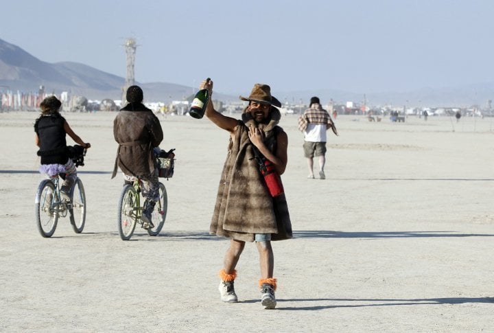 A Burning Man participant toasts the sunrise with a bottle of champagne. ©REUTERS