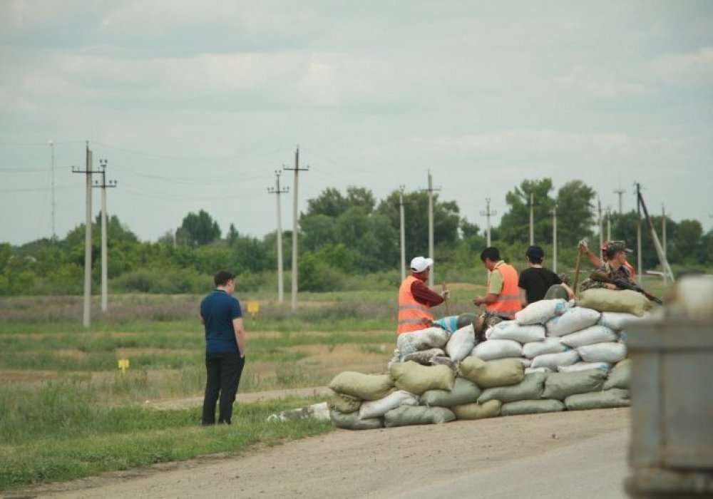 Жұмысшылар Ақтөбеден шығар жолда полицейлерге құмнан бекініс салып жатыр.