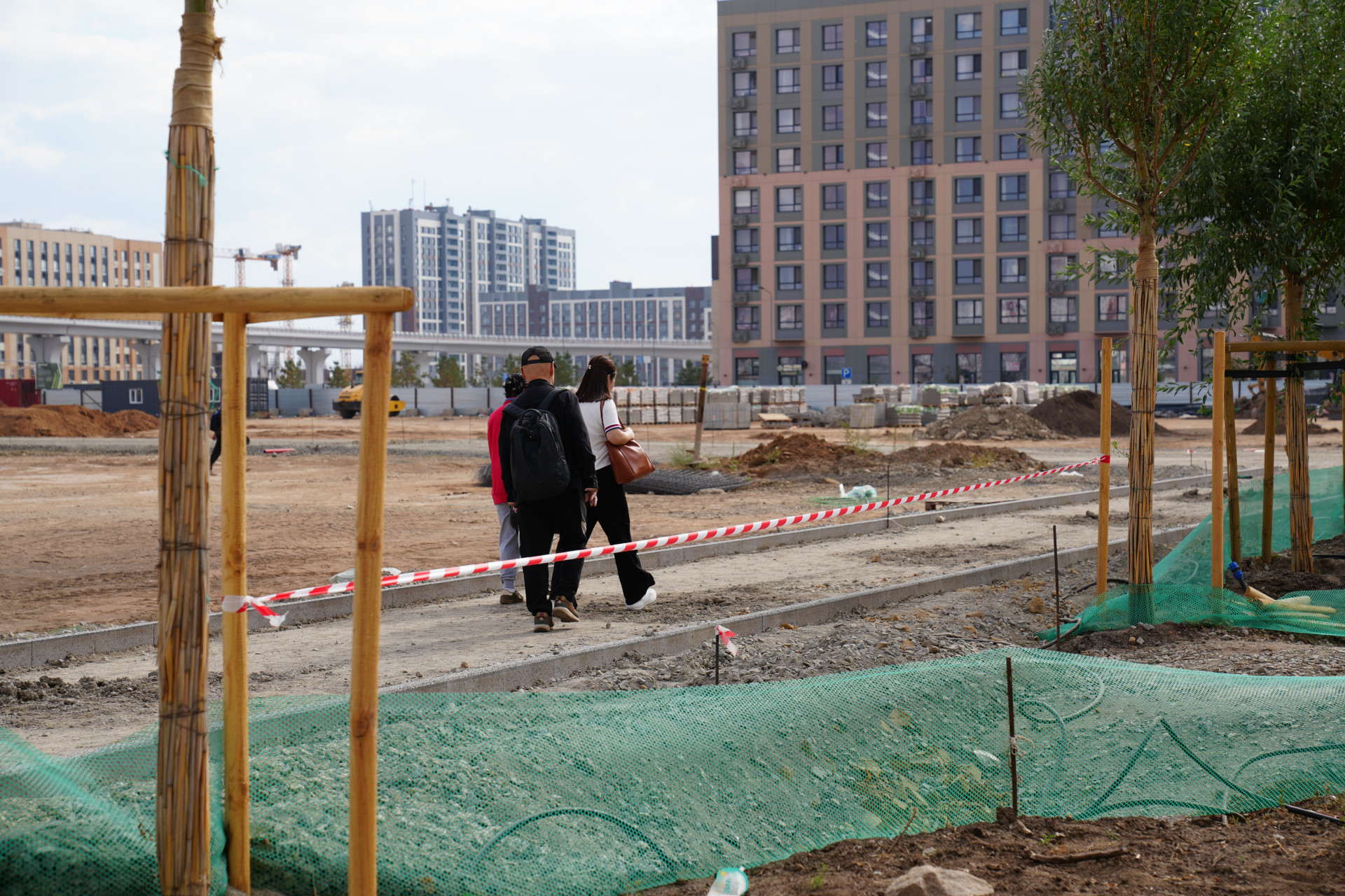 Пешеходы идут через стройплощадку на Аллее Мыңжылдық напротив вокзала "Нұрлы жол"