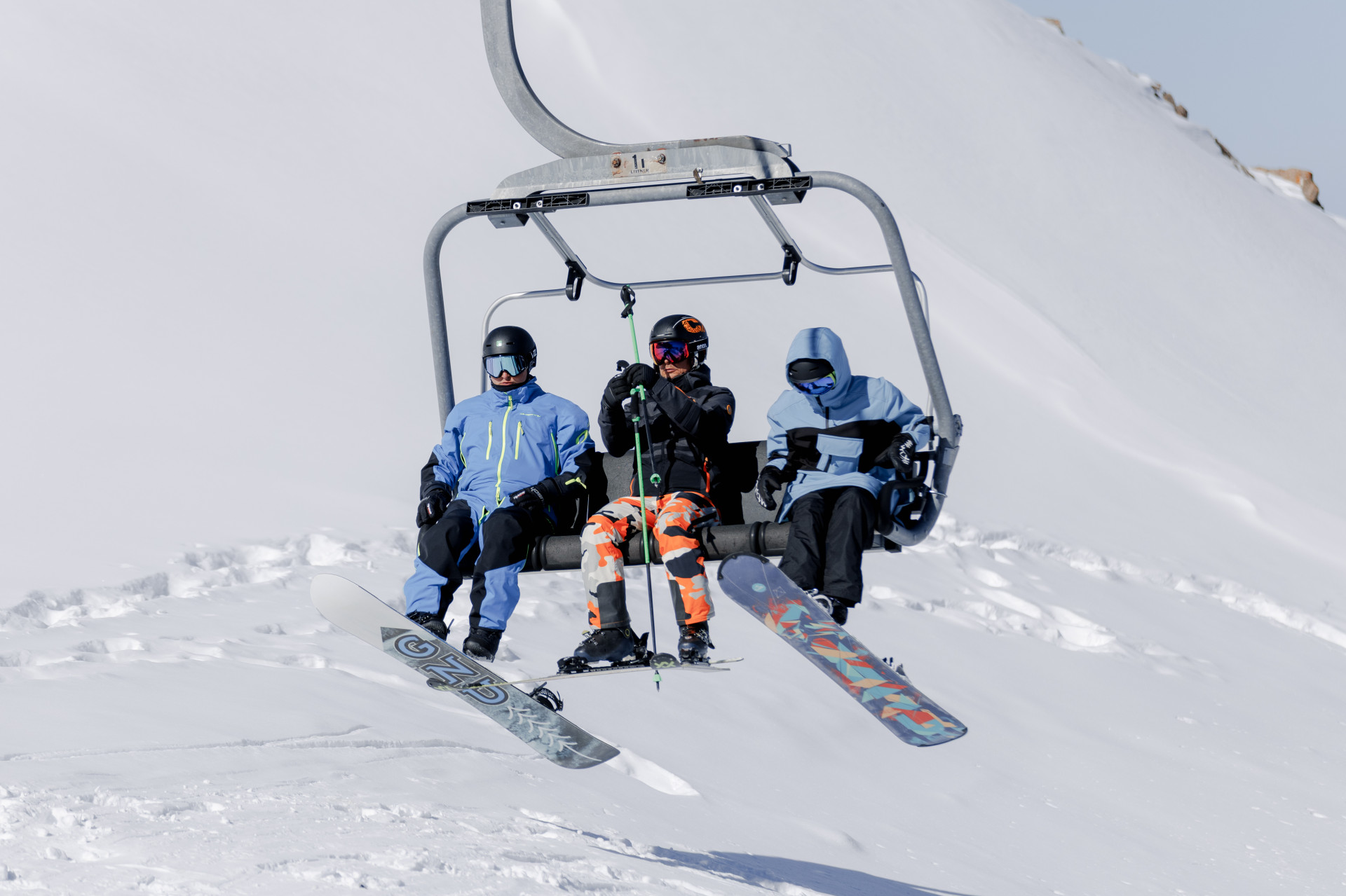 Три туриста с лыжами и сноубордами едут по канатной дороге на Шымбулак